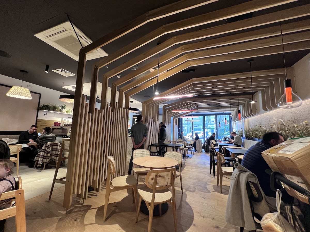 The long room at Two Children: stepped oak frames overhead, a partition of vertical oak slats, round tables, cane-backed chairs, pendant lights and a planter of dried grasses along the wall.