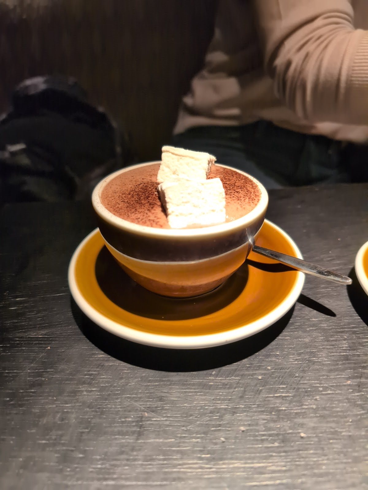 A hot chocolate dusted with cocoa and topped with marshmallows, in a striped brown and ochre cup.